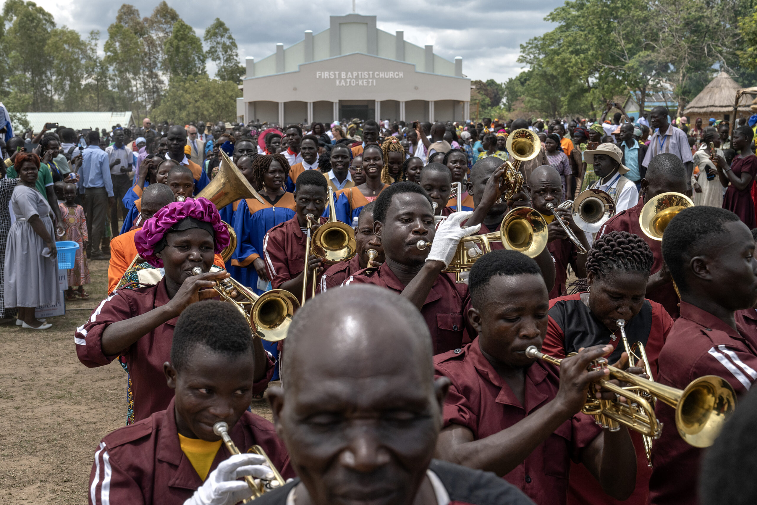 A brass band and choir lead a crowd at a Flagship dedication in front of First Baptist Church Kajo-Keji