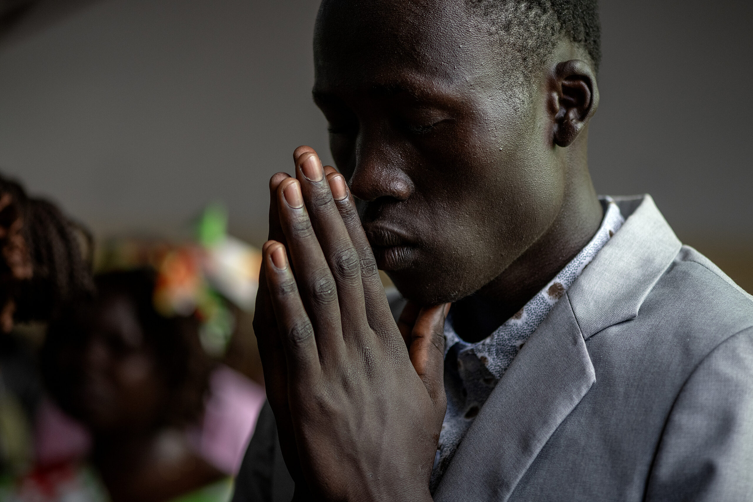 A young South Sudanese man praying with hands folded