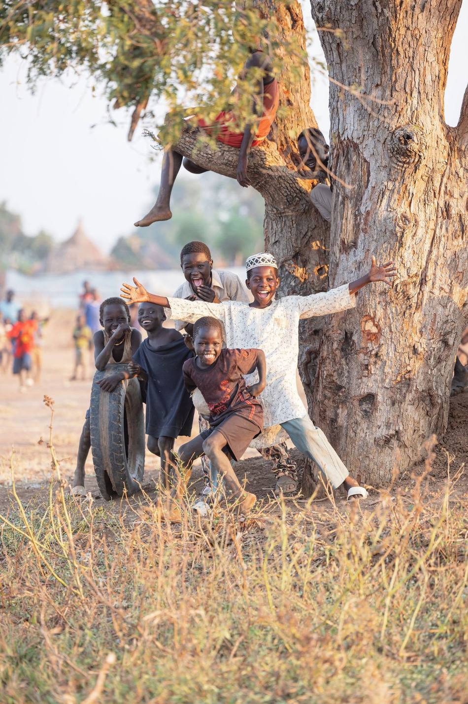 Children laughing and playing beneath a large tree in South Sudan