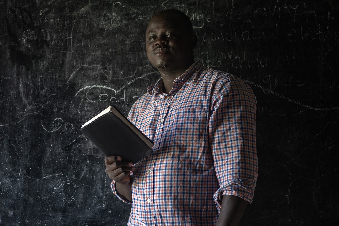 Denis Tuape, Principal of NEATS, holding a Bible in front of the classroom blackboard