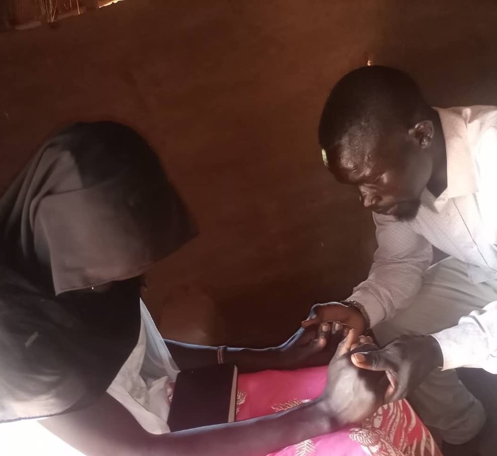 Peter, a NEATS graduate, praying with a community member in her home