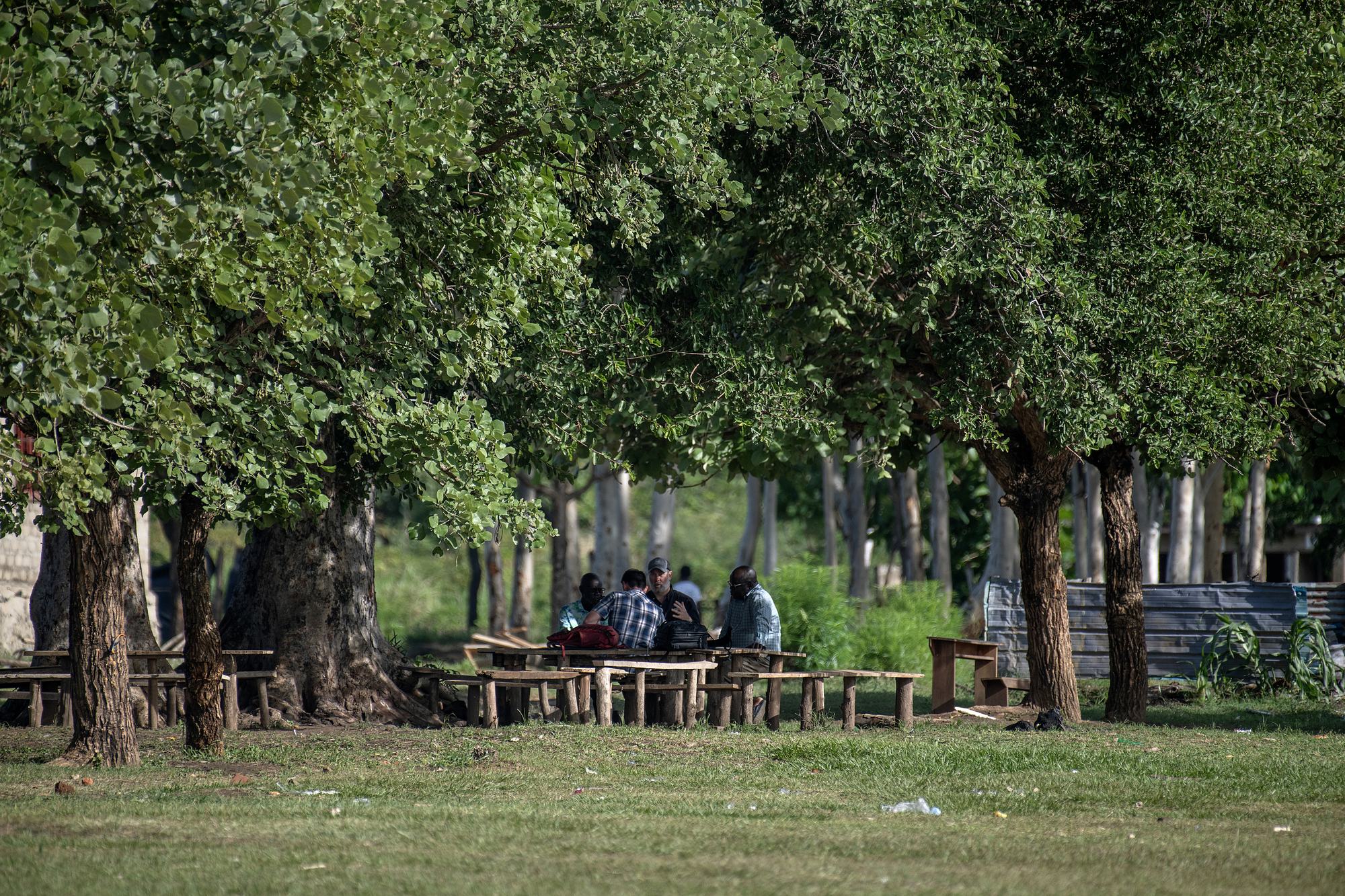 Students and leaders gathered at benches under the trees at NEATS in Kajo Keji