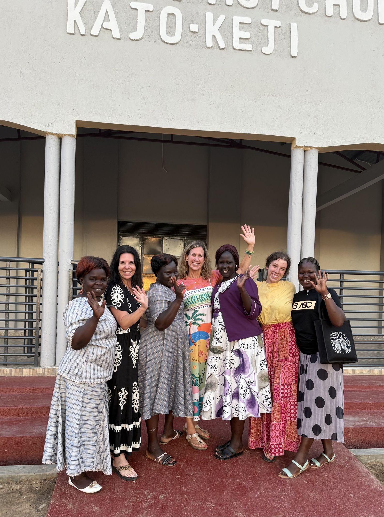 American and South Sudanese women waving together outside the church in Kajo Keji
