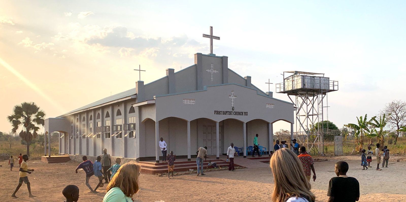 First Baptist Church Yei with its water tower, children playing out front at sunset