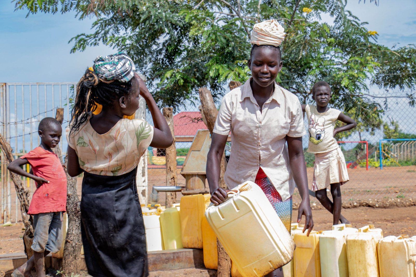 Girls carrying jerry cans of water at a community water point in the refugee-camp years